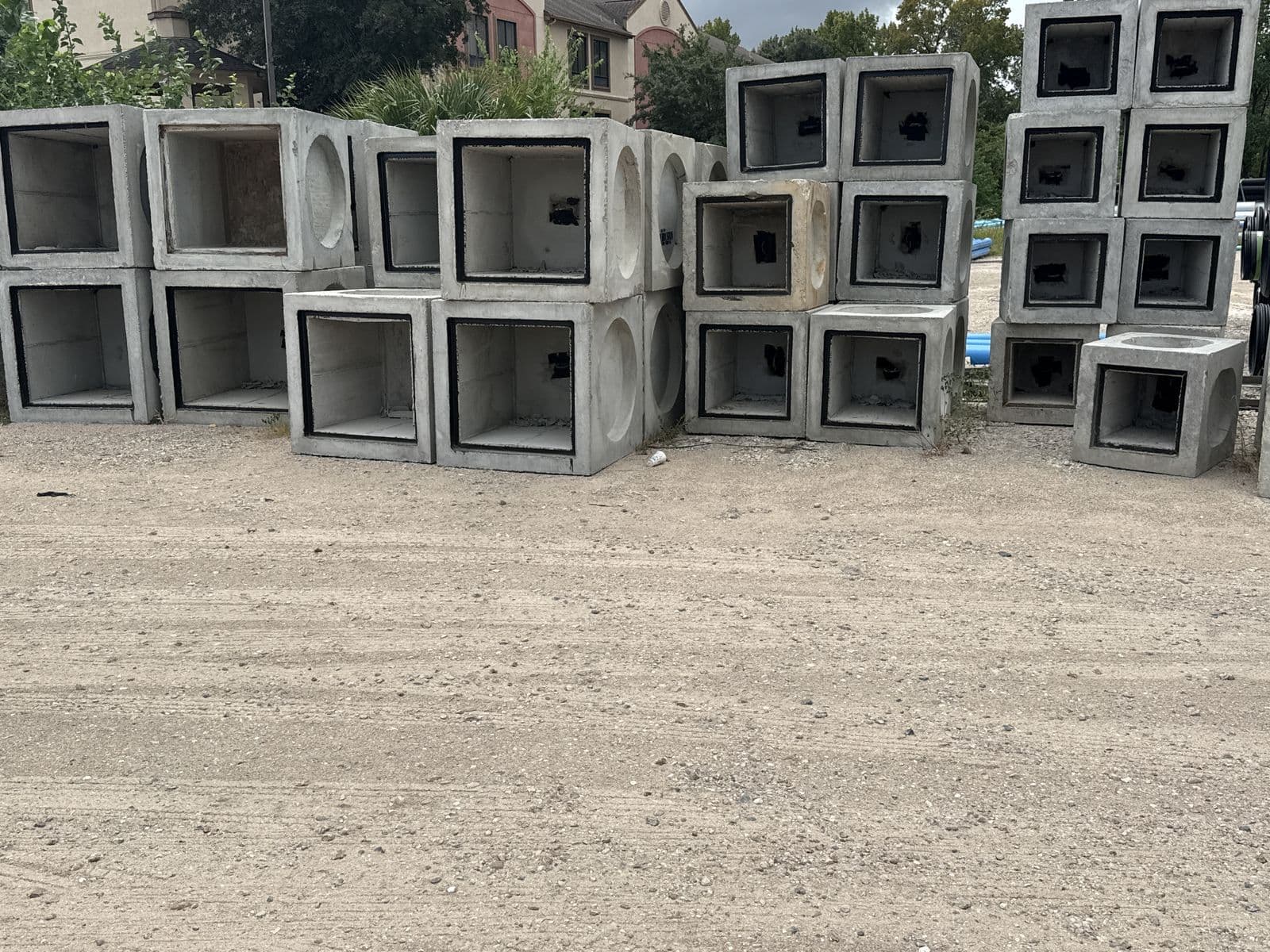 Square precast concrete catch basins with metal grates stacked in an outdoor yard